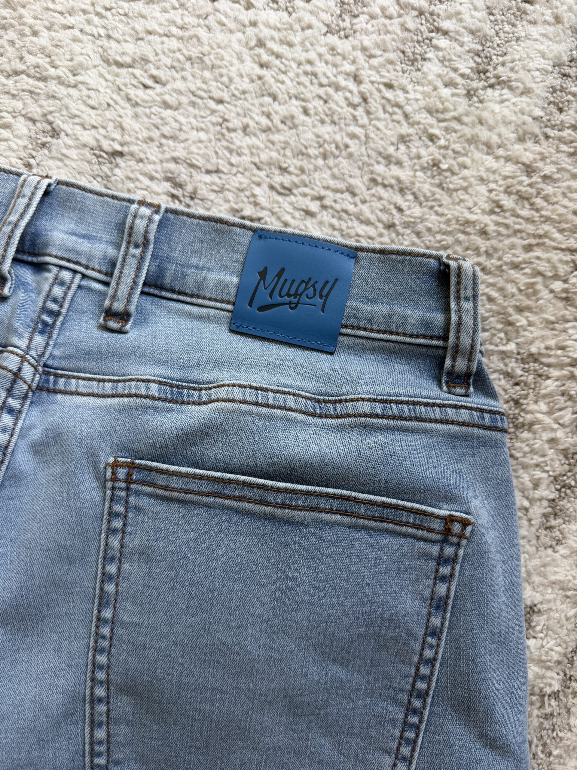 Close-up of light-wash Mugsy jeans featuring the brand’s signature blue patch on the back waistband.